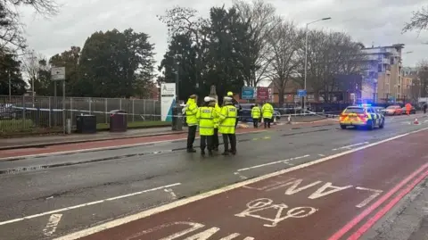 Police standing in the middle of Kings Road, with a police car in front of them and police tape covering the college's entrance.
