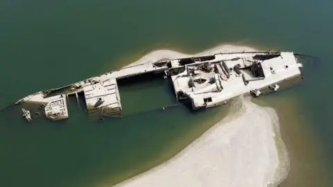 White-coloured remains of a ship sit in the Danube river.