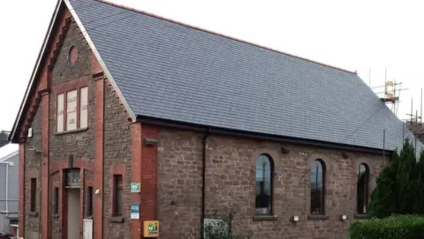 An old red brick building is seen with a new slate roof. 