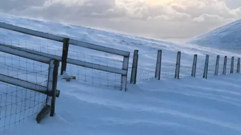 DOI A fence that is half buried in snow on the side of the Mountain Road.