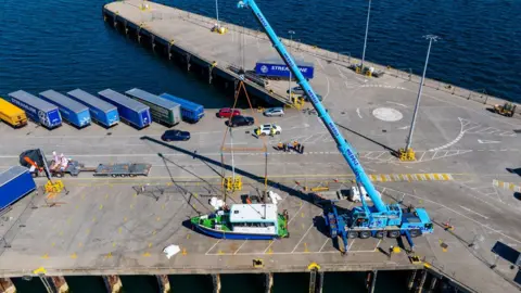 Colin Keldie/EMEC A small ferry viewed from above being lifted by a crane on dock at harbour