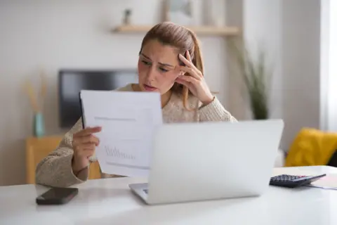 A woman with blonde hair looks at a bill