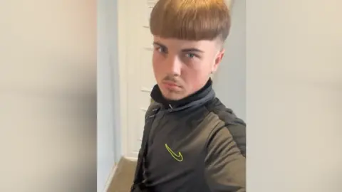 Thames Valley Police/Family handout Aidan Tottman is taking a selfie with brown hair brushed to the front of his face and shaved around the side of his head. He is wearing a Nike jumper and is stood in front of a white door