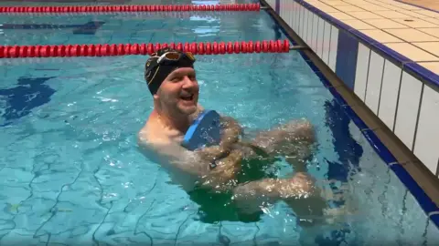 Michael Coombes smiling and holding a blue float while he is in a swimming pool.