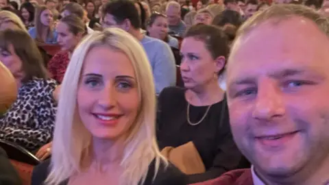 A woman and a man are sitting in the audience of a theater