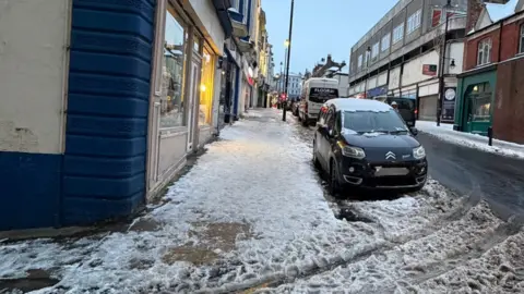 Homebird House A road in Scarborough, which is grey and mostly clear of snow, with a white-covered pavement next to it.