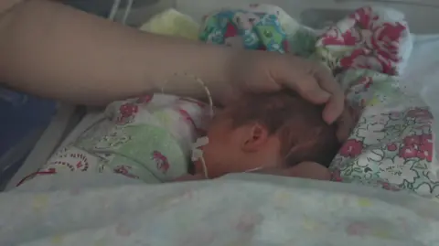 A newborn baby sleeps peacefully, with a parent's hand stroking her head 