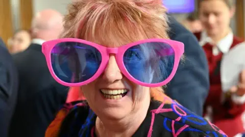 Getty Images Christine Grahame, with her trademark spiky, coloured hair, beams at the camera while promoting breast cancer awareness month, wearing giant pink glasses.