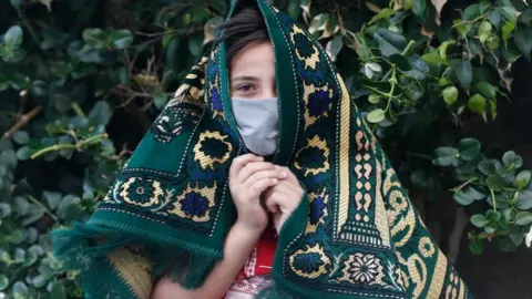 Getty Images A young Palestinian wearing a face mask holds a prayer mat over their head