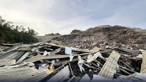 Collapsed sheets of metal strewn in front of a mountain of rubbish