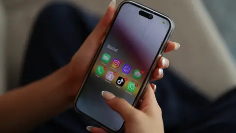 Reuters Two hands holding a mobile phone which is displaying social media apps including Instagram, TikTok and Snapchat.