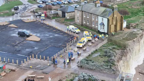 Eddie Mitchell Emergency service vehicles are parked in a cliff-top car park. 