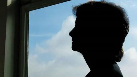 Silhouette of a woman's head and shoulders against a window showing blue skies.
