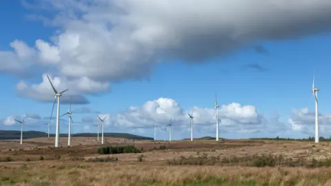 Getty Images Windmills in a field. It's a cloudy day.