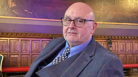 Barry Mackleston Barry in a three piece suit and clear glasses. 