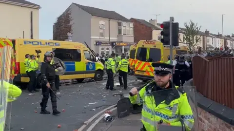 PA Yellow riot police vans and officers in riot gear and high-vis yellow jackets, on a street in Southport during the unrest