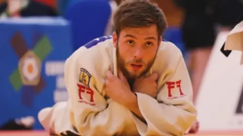 European Judo Union Rowan Kinsella in judo kit lying propped up on his elbows in a judo arena 