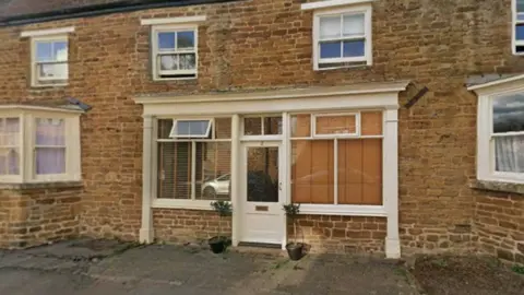 A two-storey brick cottage with white sash windows either side of a white window-framed door facade.