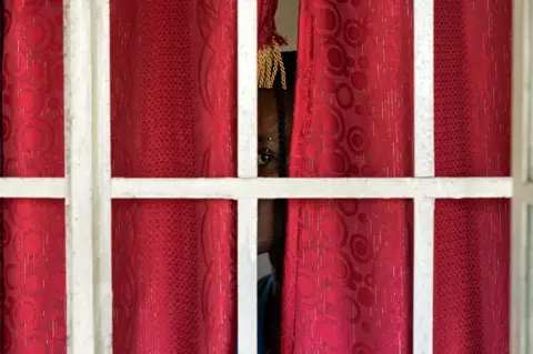 Lee Price Person peeking through a pair of closed red curtains