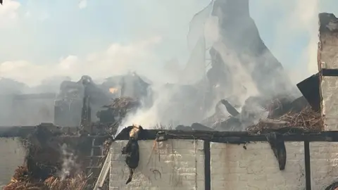 Close up of badly damaged thatched roof with smoke in the air