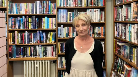 Shariqua Ahmed/BBC Jennie Storey wearing a black cardigan and white dress - looking at the camera.