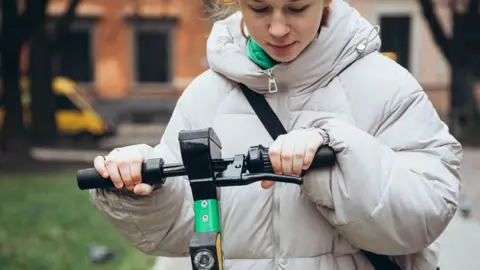 Close up of a young girl wearing a coat holding onto the handles of an electric scooter 