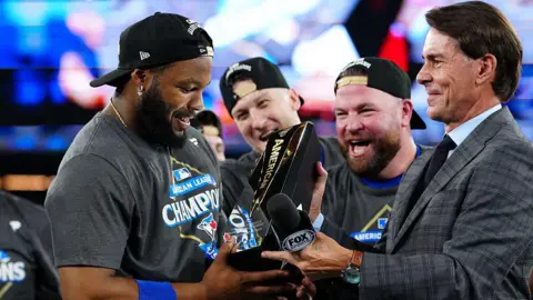 Getty Images Vladimir Guerrero Jr. No. 27 of the Toronto Blue Jays receives the Leland S. MacPhail Award as American League Championship Series Most Valuable Player after winning Game 7 of the American League Championship Series presented by LounDepot between the Seattle Mariners and Toronto Blue Jays at Rogers Center in Monday, October 20, 2025 in Toronto, Ontario, Canada. He's surrounded by his teammates, all wearing American League Championship Series jerseys. He looks at the trophy lovingly.
