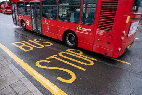 Getty Images A red London bus pulls into a bus lane, indicated by yellow lines and 'bus route's painted on the road surface with yellow paint.