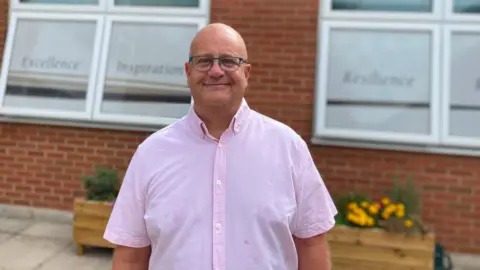 Simon Grieff stands in front of the school smiling at the camera