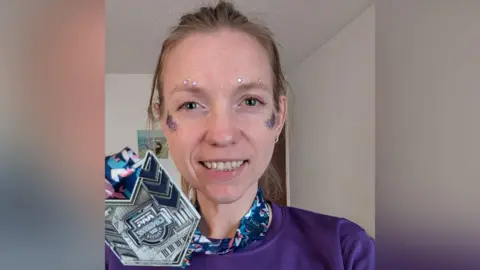 West Suffolk NHS Foundation Trust Ceiridwen is in a room with white walls. Her head and shoulders are visible. She is wearing her purple My Wish running t-shirt and is holding her silver medal close to her face