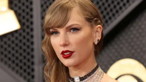 Reuters Taylor Swift wearing red lipstick and two earrings stands in front of a black and gold background