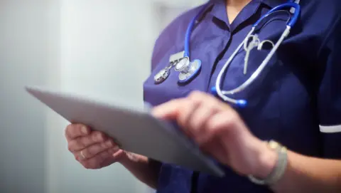 A woman in blue hospital uniform with a clipboard