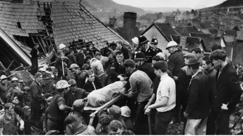 Getty Images Black and white photo of emergency workers carrying out a body on a stretcher 