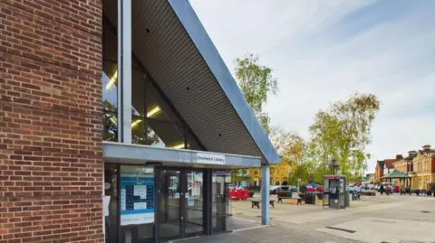 Worcestershire County Council A red brick building with a long sloped metal roof. A sign says Droitwich Library