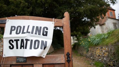 A polling station sign on a gate outside a polling station set up at All Saints Church in Monk Sherborne, Hampshire