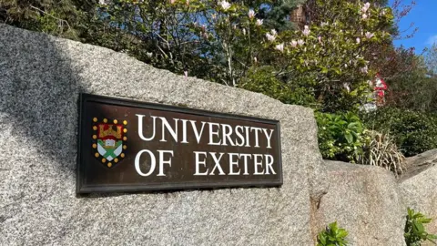 The University of Exeter sign set in granite and with shrubbery around the outside.