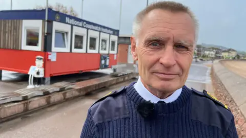 David wearing navy blue uniform and standing in front of the coast watch cabin.
