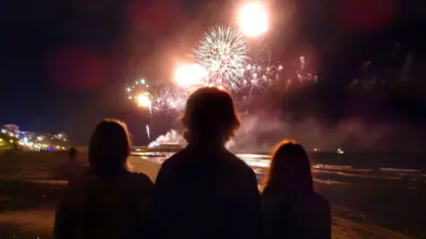 Getty Images Three people in silhouette against the night sky standing on Bournemouth beach fireworks. 