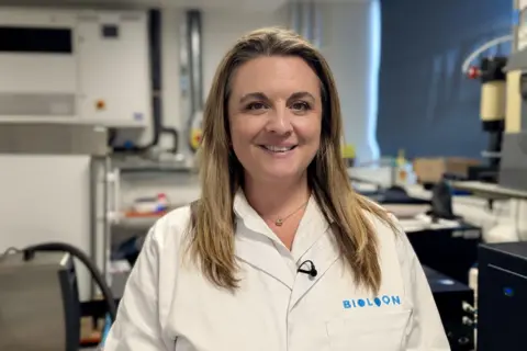 A woman in a lab coat smiles at the camera