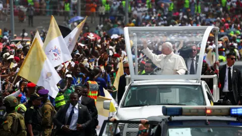 Reuters Pope in his vehicle on the right, waving to crowds that are on the left of the picture