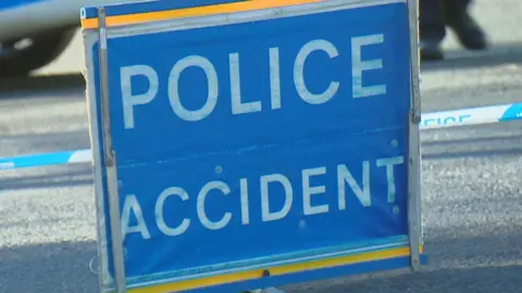 Police accident sign with white block capitals on blue sign, with road behind.