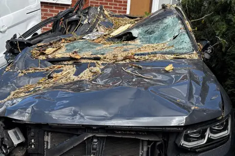 A grey car that is crumped and covered in debris