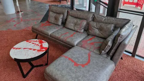 Grey L-shaped sofa and small round coffee table sprayed with red paint.
