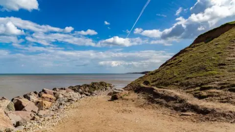 Mappleton beach, there is a cliff and some rocks. It is a sunny day.