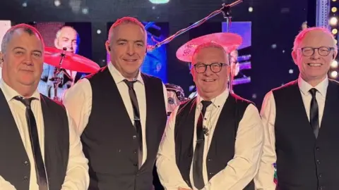 Four men in waistcoats and ties smiling at the camera.