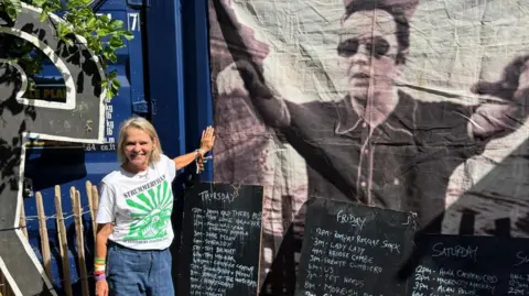 Lucinda Tait stands next to a large photo printed on fabric of her husband Joe Strummer.