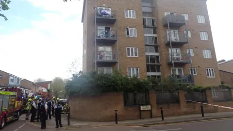 London Fire Brigade Yellow brick block of flats with police and fire engines to the left. One third floor window is bent out of shape