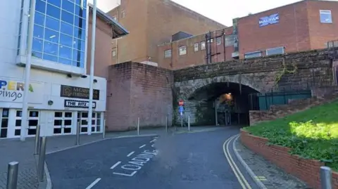 A general view of the tunnel at Ladies Walk in Workington. It is next to a large white building with signs for Opera Bingo and The Ritz cinema. A road runs above the tunnel, with other red-brick buildings in the background.
