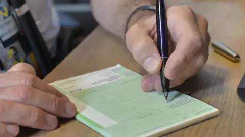 A close up of a GP starting to fill out a green prescription on a  pad with a pen.