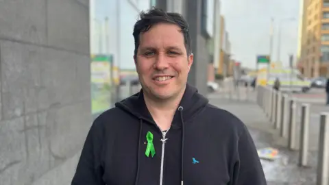 A man wearing black clothing smiles at the camera